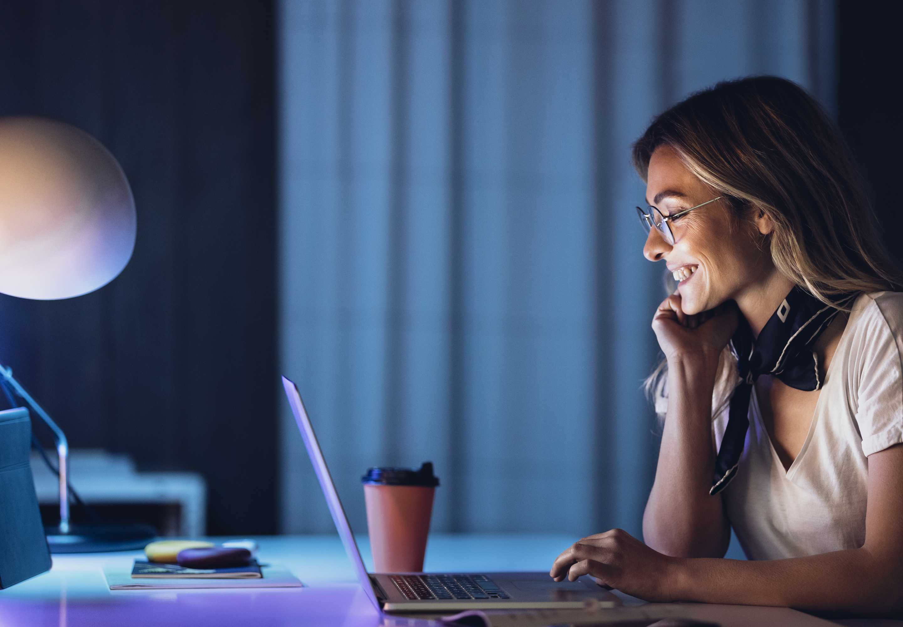 smiling woman sitting at desk working on laptop