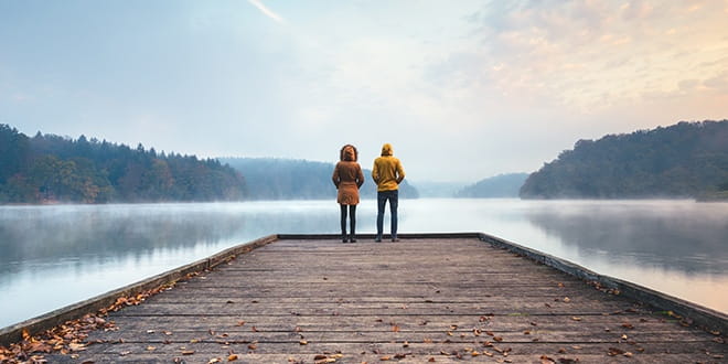 Two people standing at the end of a dock overlooking a lake